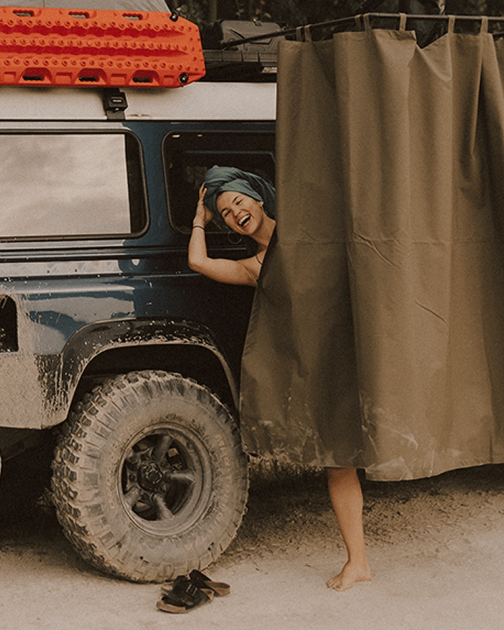 Véhicule tout‑terrain avec galerie de toit et cabine de douche ou d’intimité montée sur le côté en extérieur.