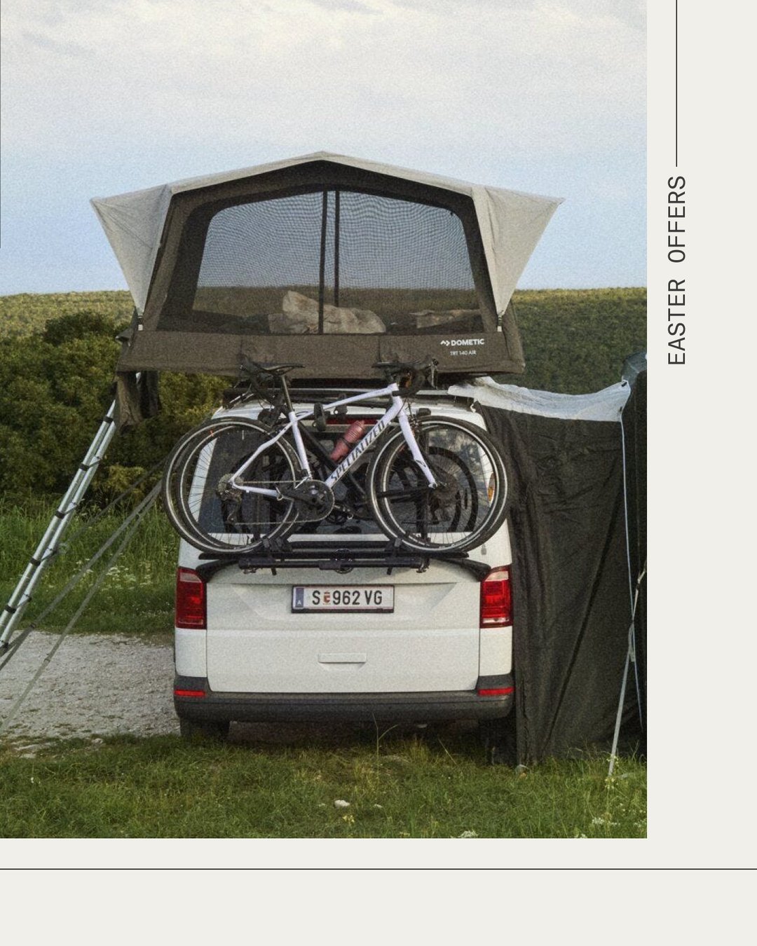 Taktält monterat på ett fordon i en bergsmiljö, med en hund i tältöppningen och en person som håller i stegen.