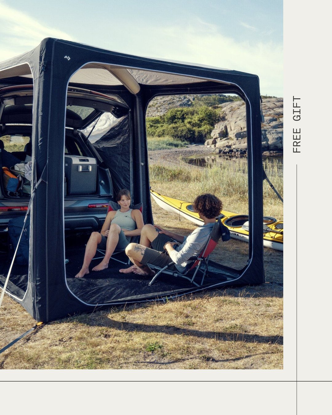 Dometic HUB-shelter gekoppeld aan een voertuig, met twee personen in kampeerstoelen en een kajak bij een kustkampeerplek.