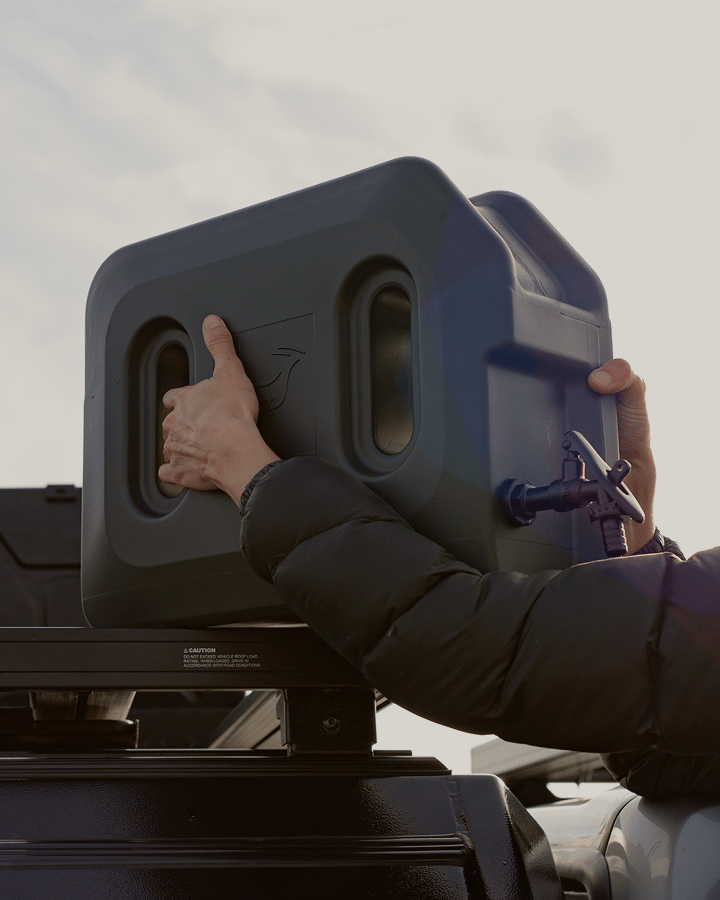 Une personne place un conteneur d’eau ou de carburant sur une plate‑forme de galerie de toit.