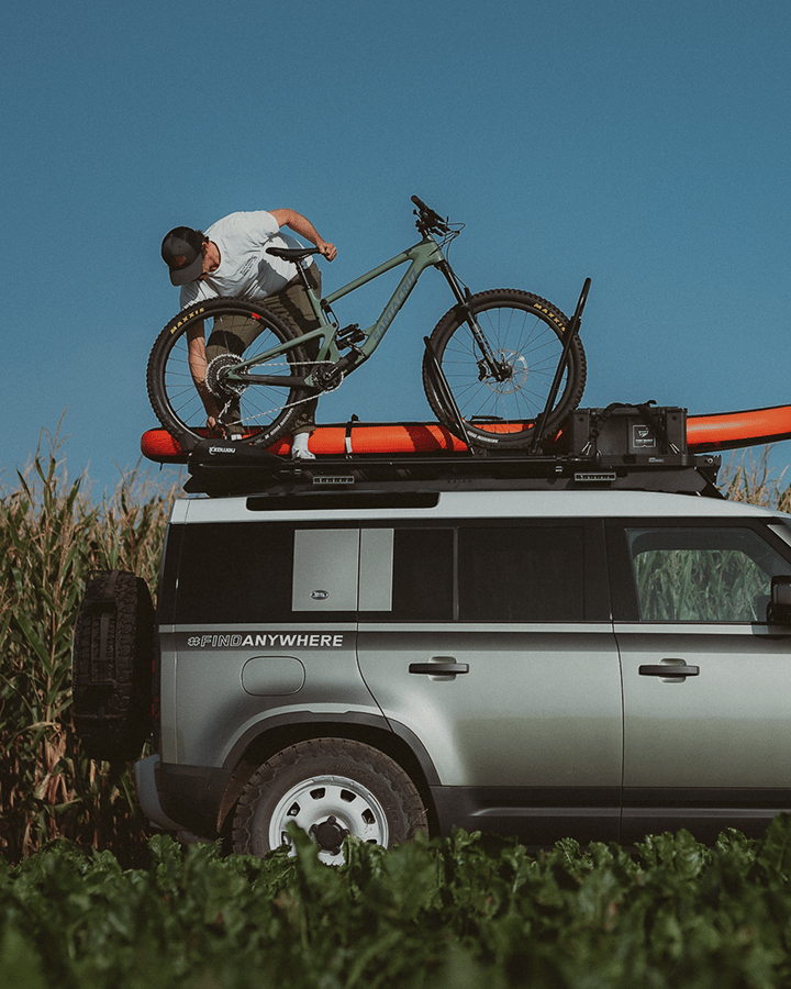 Une personne charge un vélo sur une galerie de toit transportant un kayak et du matériel.