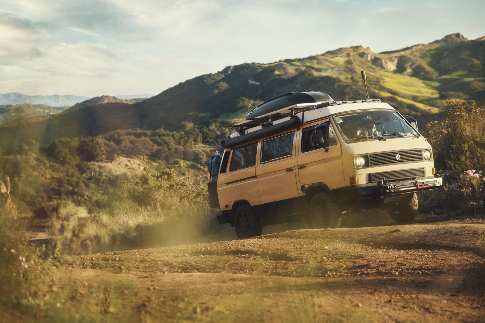 An old school yellow VW van driving up a dirt hill. 