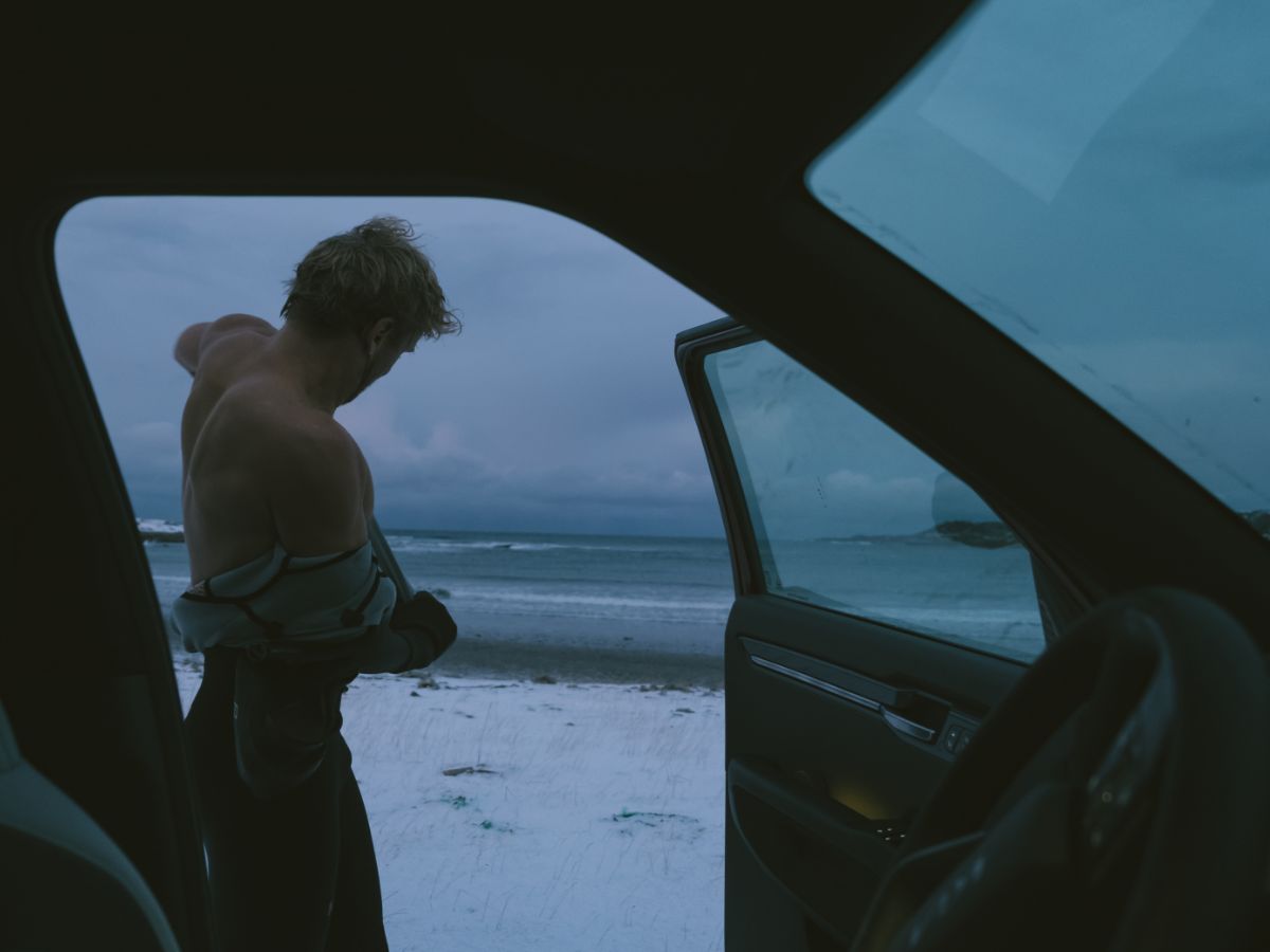 An image through the car of a person putting on a wetsuit on a cold, snowy beach  