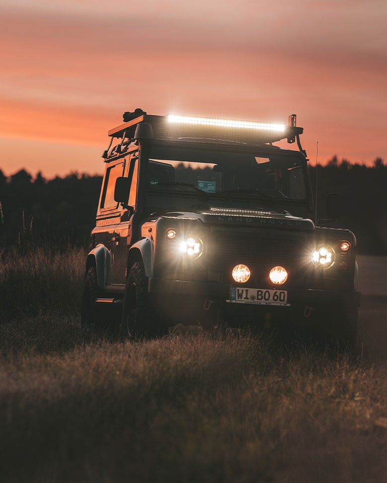 Veicolo fuoristrada Land Rover equipaggiato con barra LED Front Runner Dometic, che illumina un percorso al tramonto durante un’avventura di overlanding.