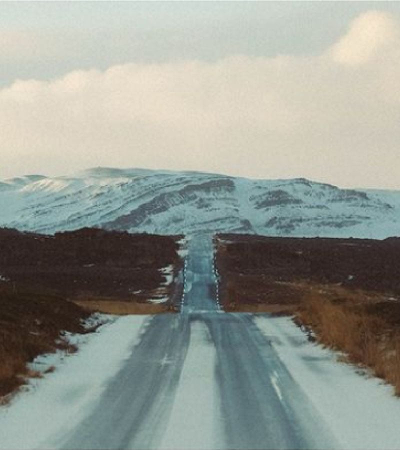 A long icy road stretching into the distance that leads to snow-covered mountains under a cloudy sky
