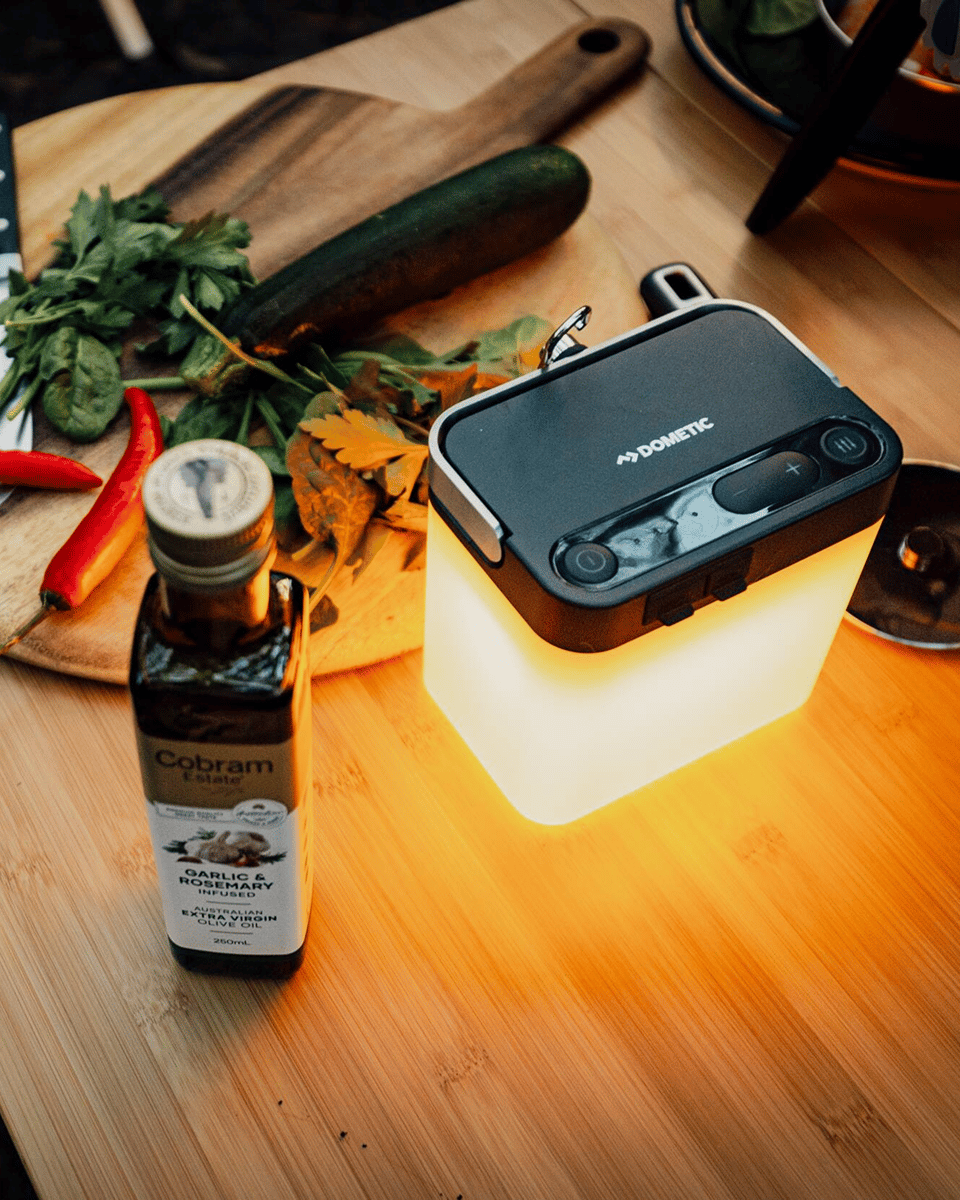Lampe Dometic GO Area Camp Light éclairant un espace de cuisine outdoor avec des ingrédients frais sur une table de camping