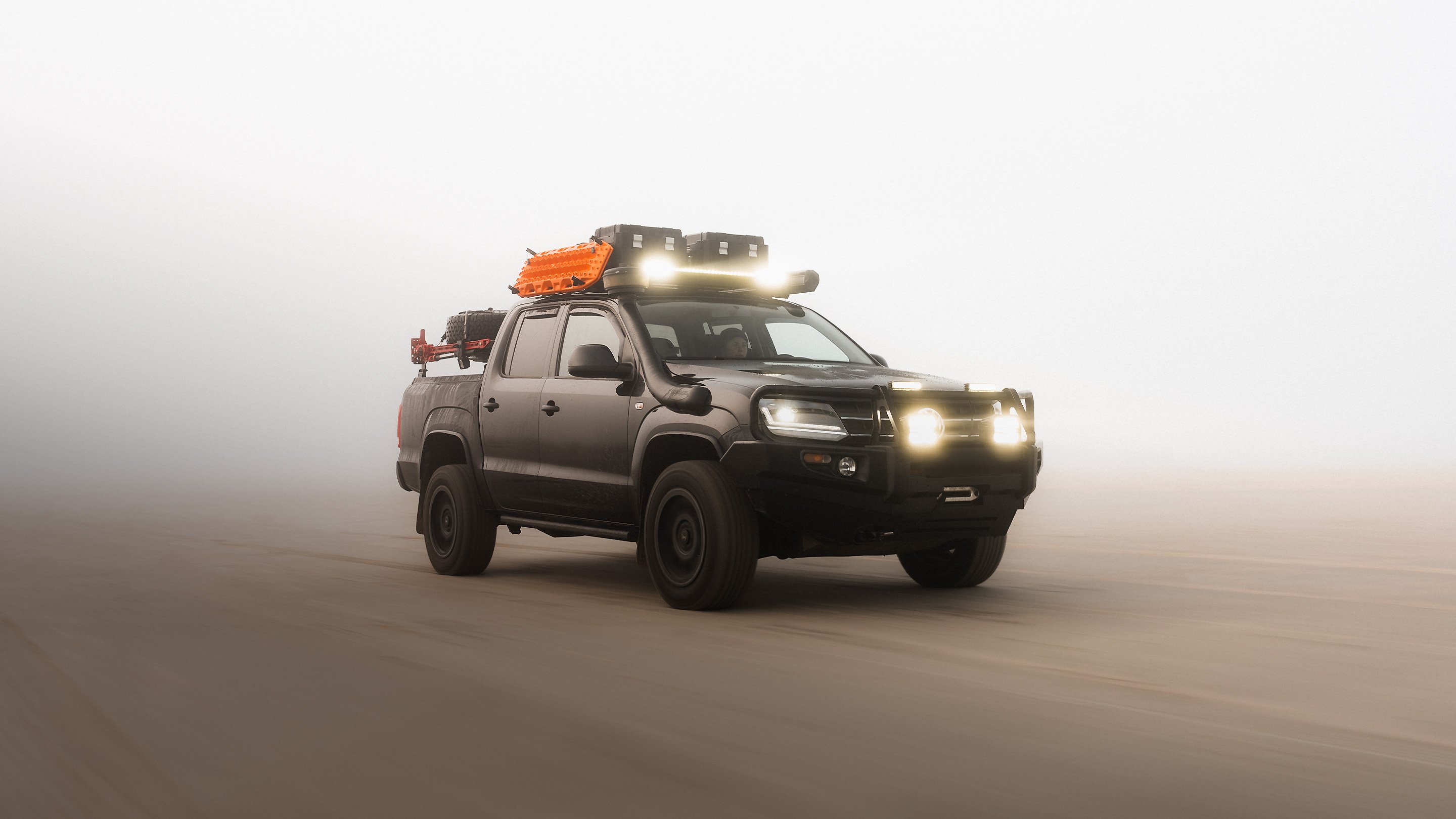 Pickup truck equipped with a roof rack, LED light bar, recovery boards and storage boxes driving in dusty off-road conditions