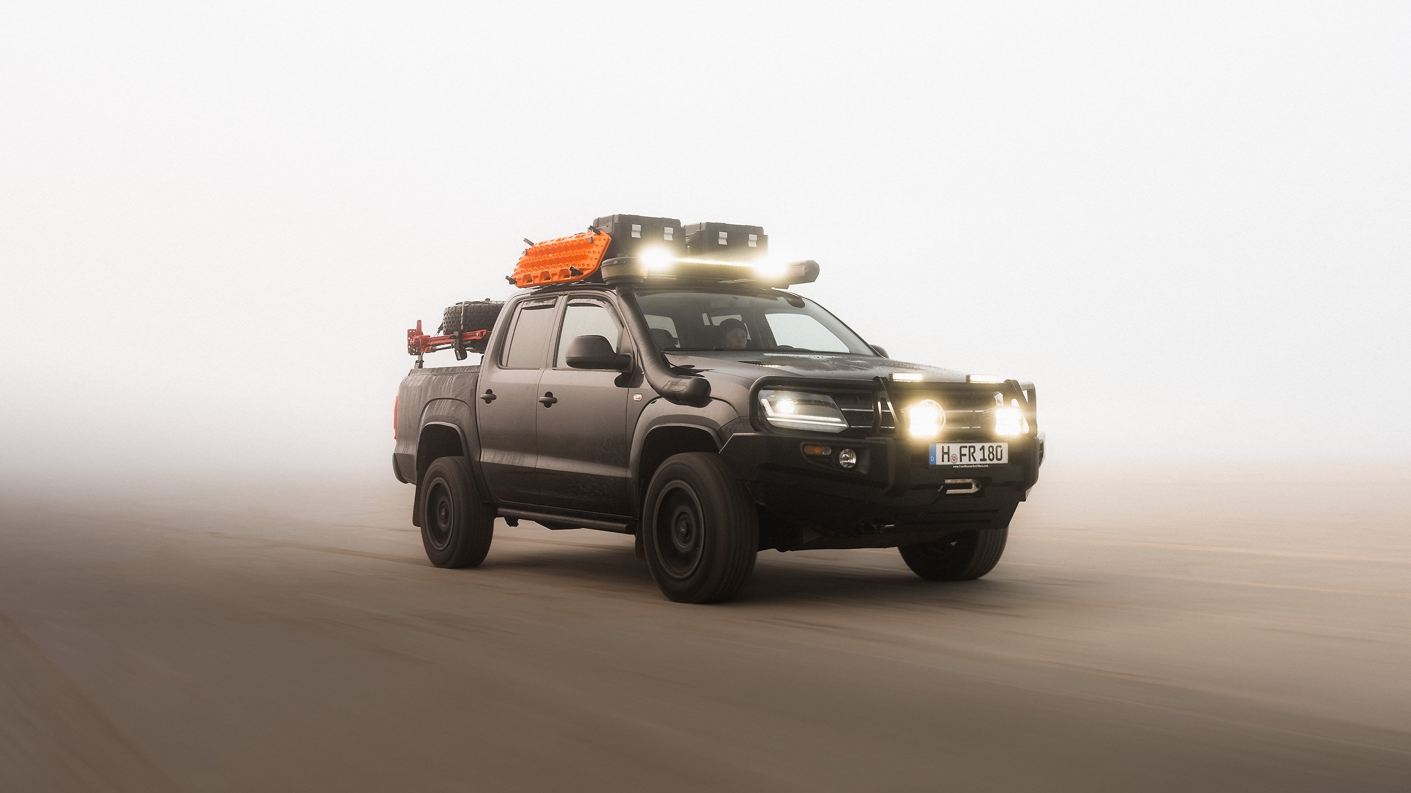 Pick-up équipé d’une galerie de toit, d’une barre lumineuse LED, de plaques de désensablage et de boîtes de rangement roulant dans des conditions tout-terrain poussiéreuses