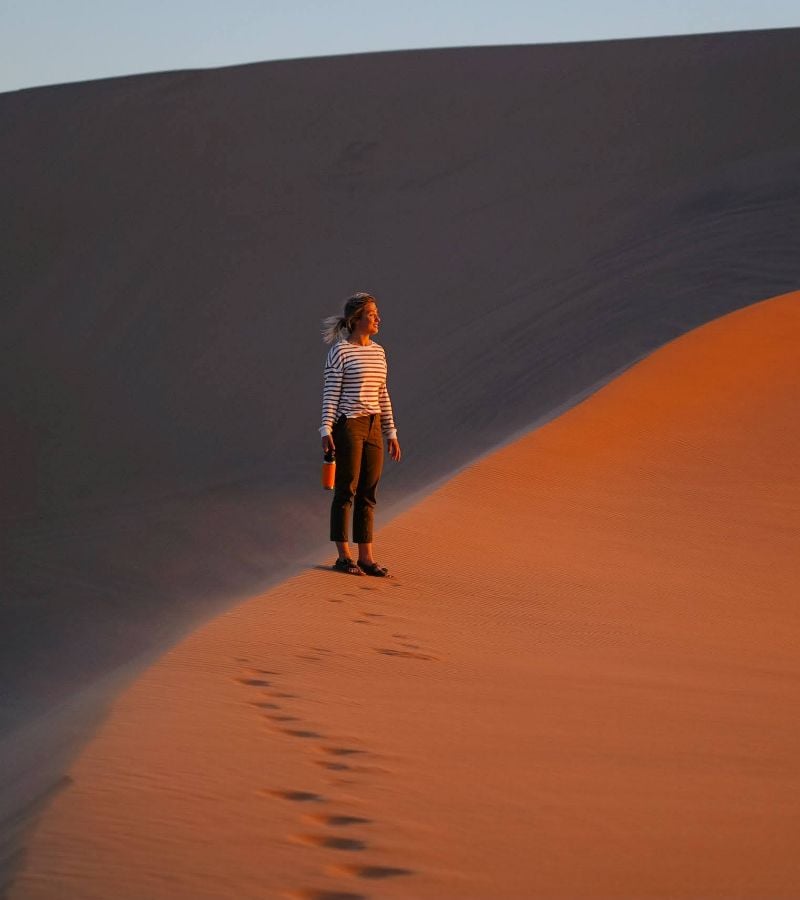 A woman standing alone in a vast desert with golden sand