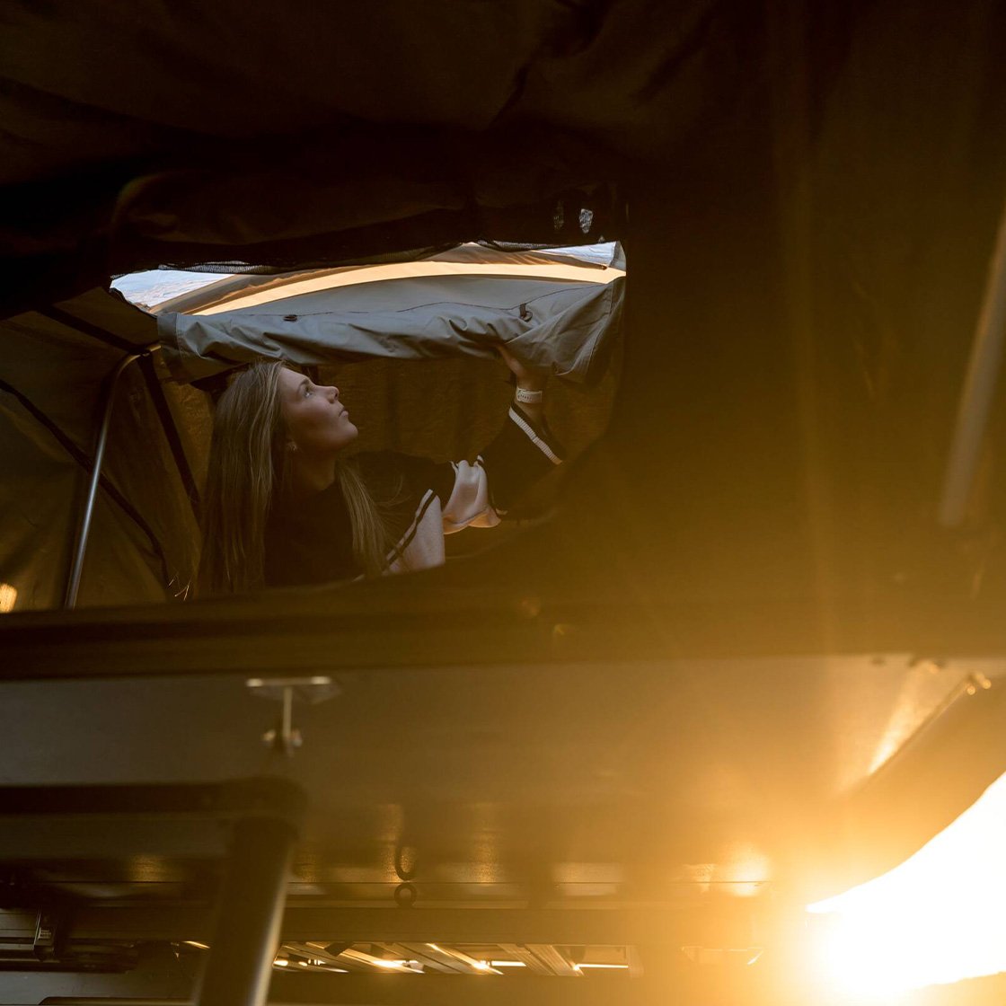 Persona all’interno della tenda da tetto Front Runner Dometic Feather‑Lite II che apre la finestra panoramica al tramonto.