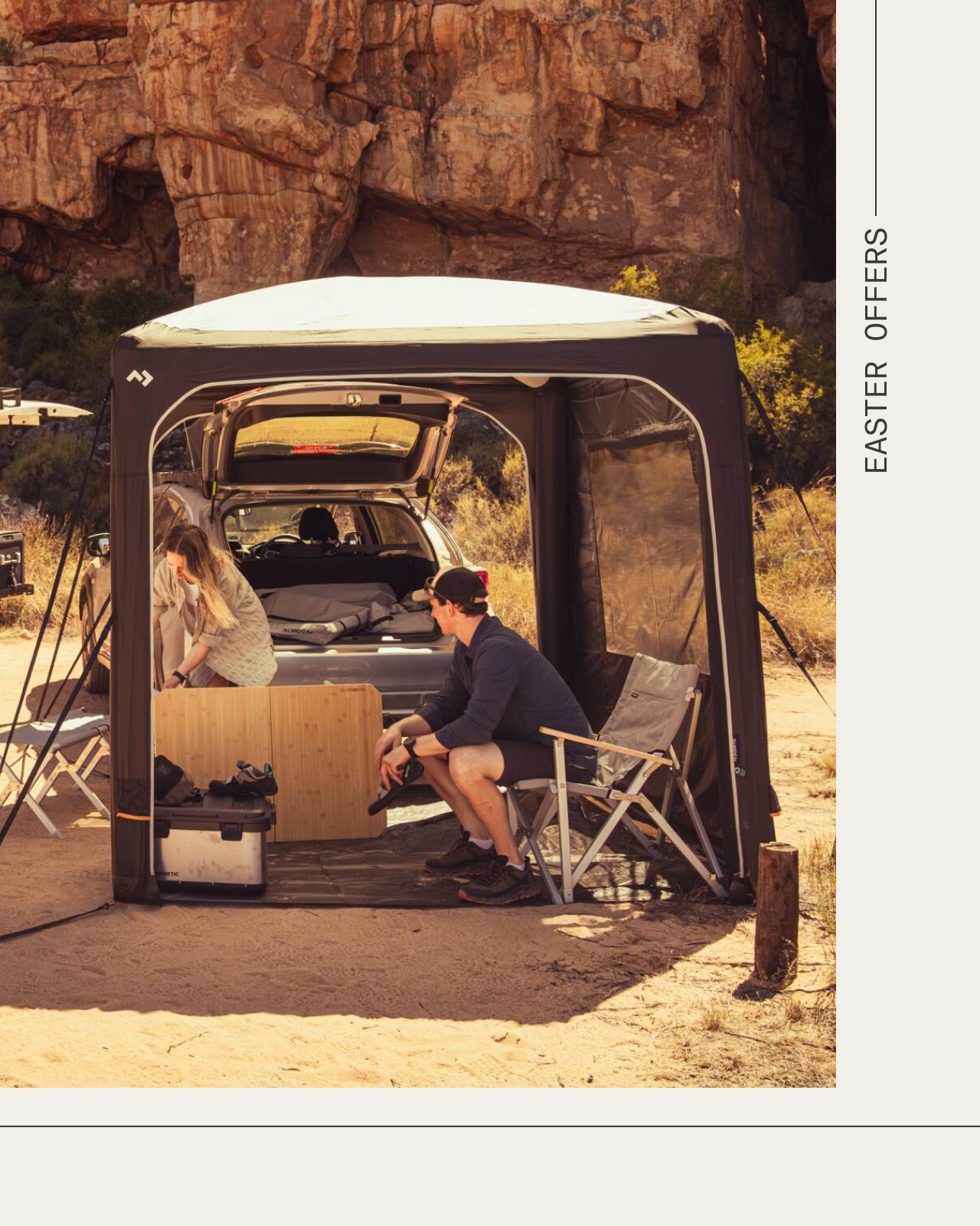 Abri Dometic HUB fixé à un véhicule, créant un espace de camping ombragé avec deux personnes et du matériel outdoor dans un décor rocheux.