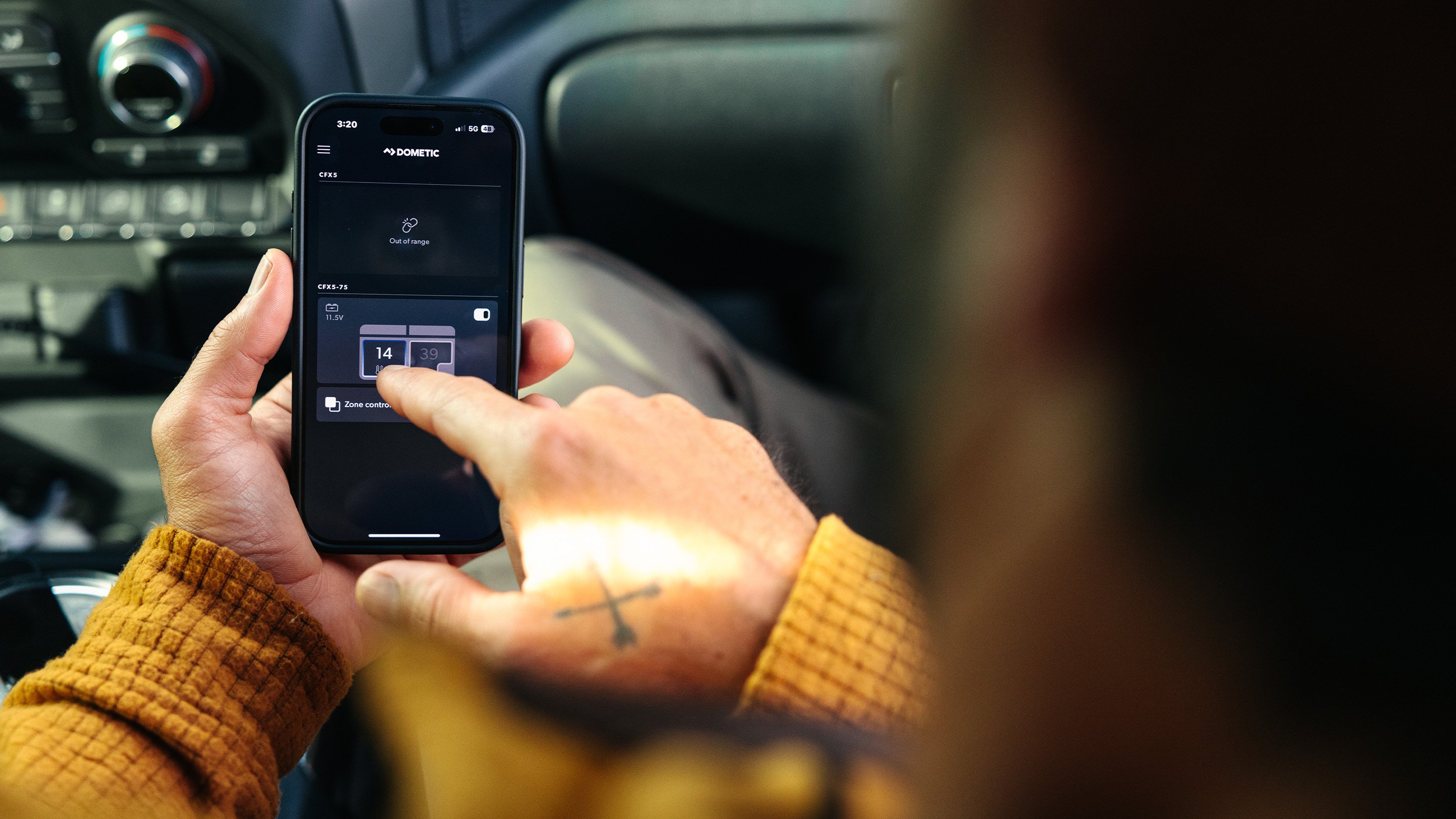 Person using the Dometic mobile app inside a vehicle to monitor and control a connected portable cooler.