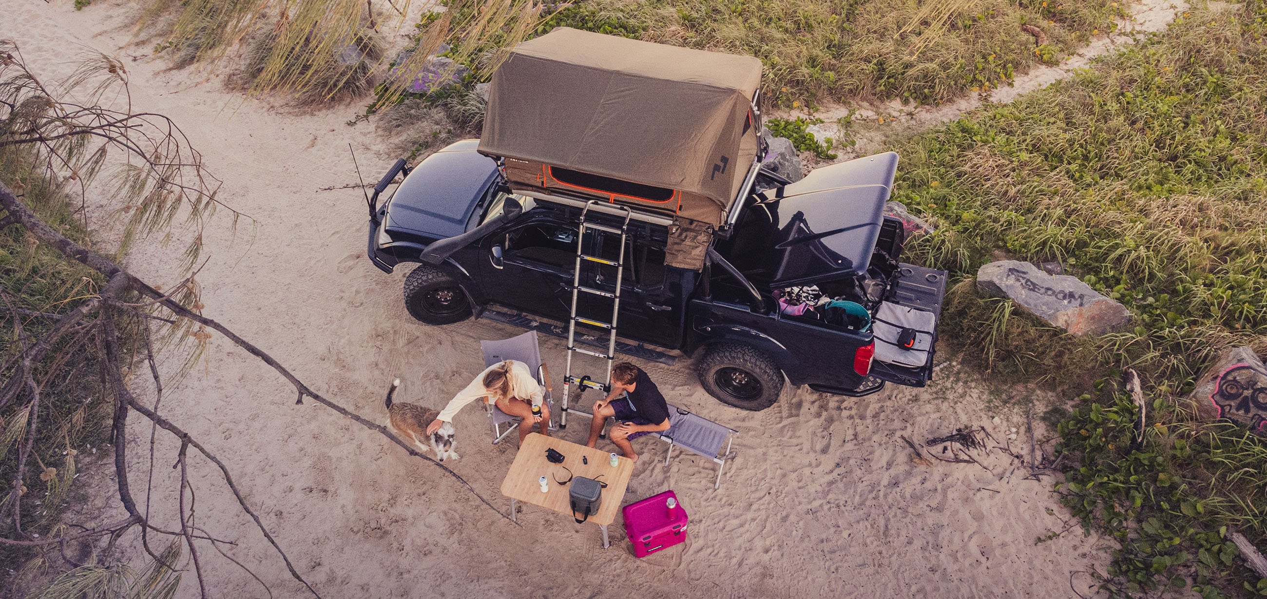 Couple sitting outside their camper petting a dog.