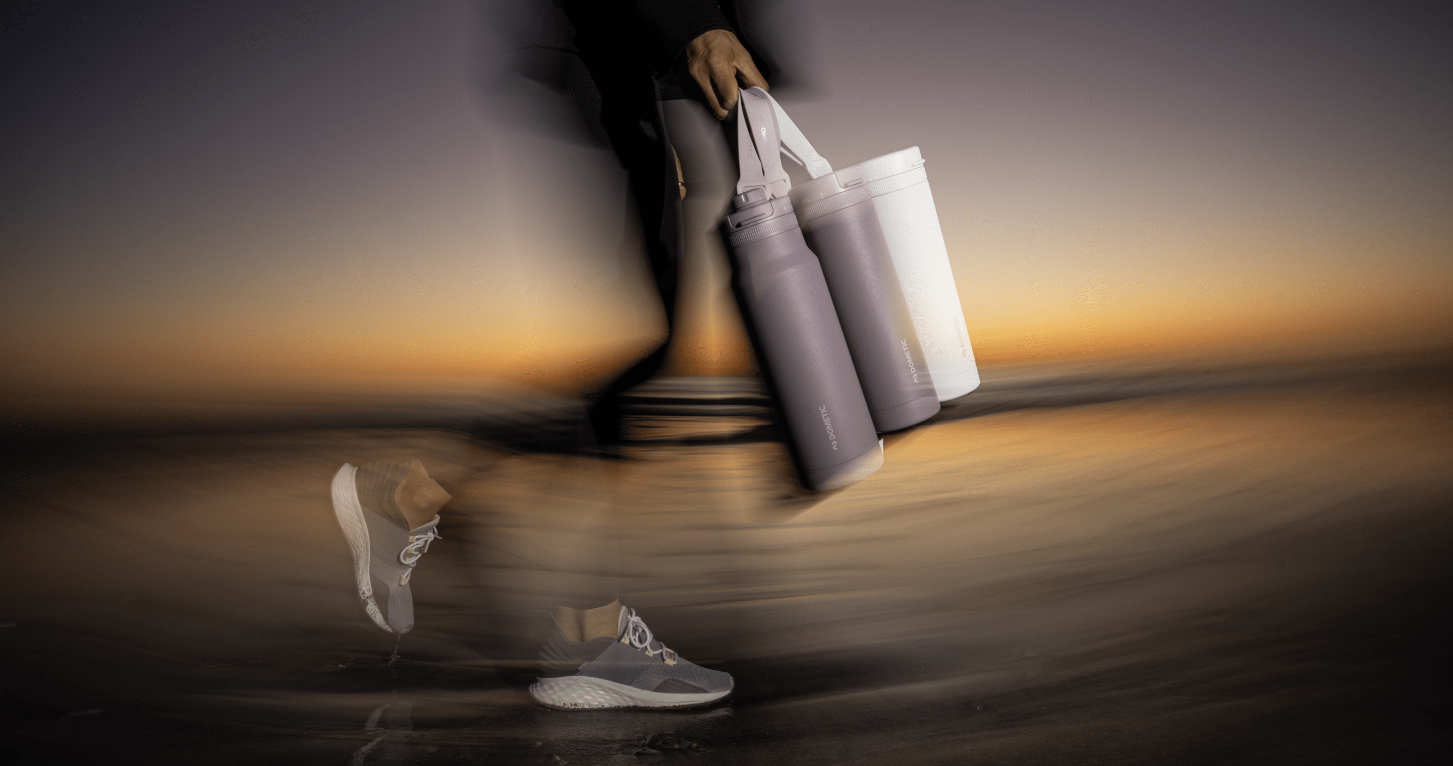 Person walking holding purple and white drinkware items by straps.