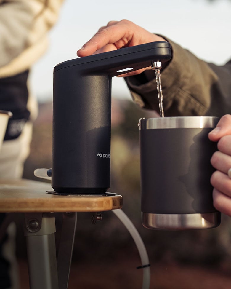 Dometic GO Hydration Water Faucet dispensing water into an insulated mug at a campsite, portable water solution for outdoor adventures