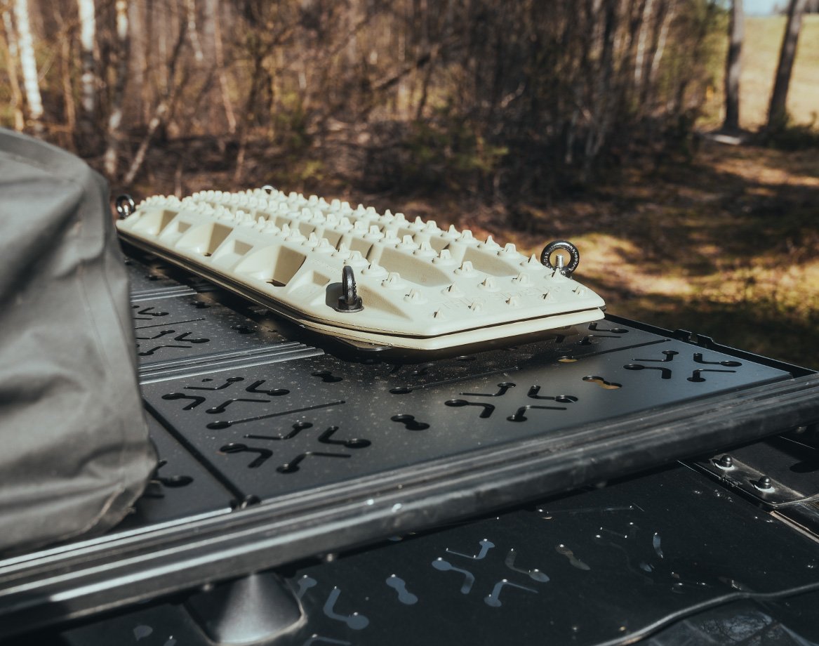 Gros plan de recovery boards montés sur une galerie de toit avec panneaux de decking dans un environnement forestier, avec du matériel outdoor à proximité.