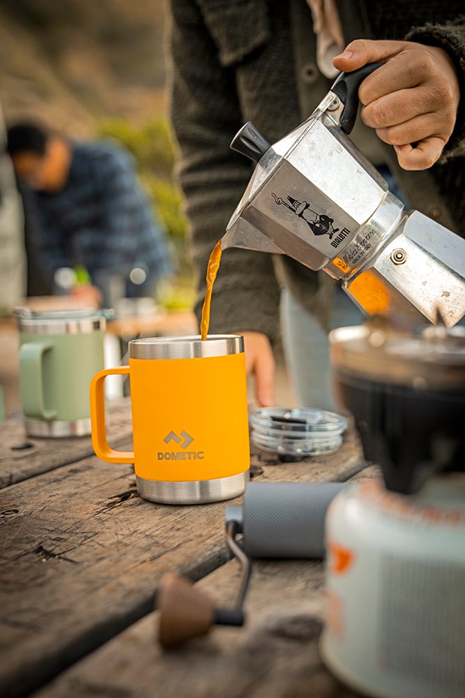  Someone pouring coffee from a percolator into a Dometic mug.