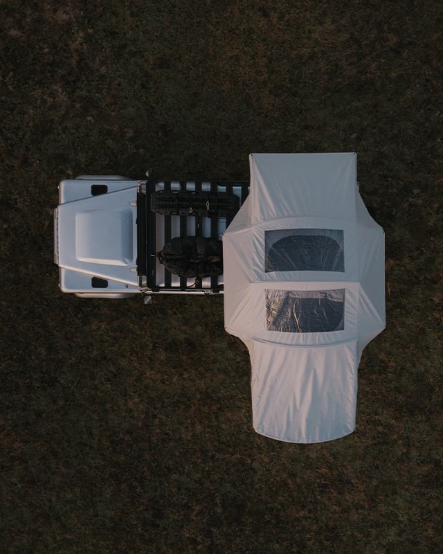 Top‑down view of a vehicle with a fully opened Front Runner Dometic Feather‑Lite II rooftop tent set up in an outdoor field.