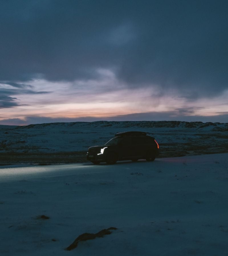 A dark silhouette image of an SUV on a snowy landscape with a dusk sky,
