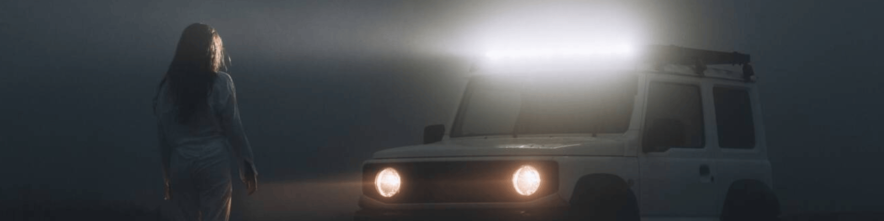 Woman in darkness standing in headlights of white Jimny.