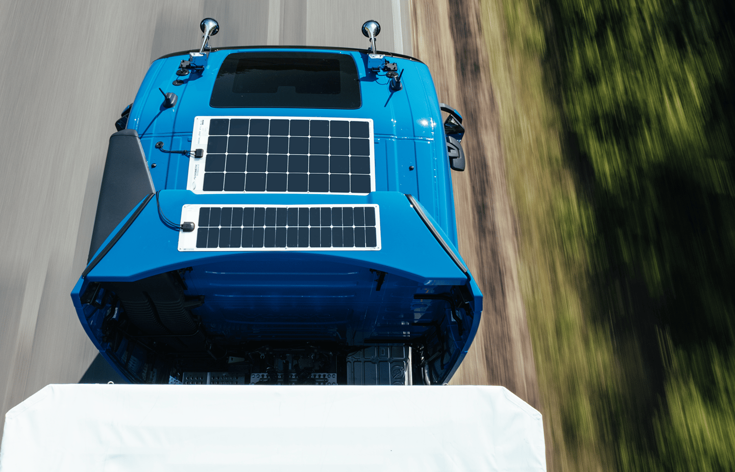 Blue Truck with Solar panels on cabin driving on the road, fotographed by a drone above the trailer