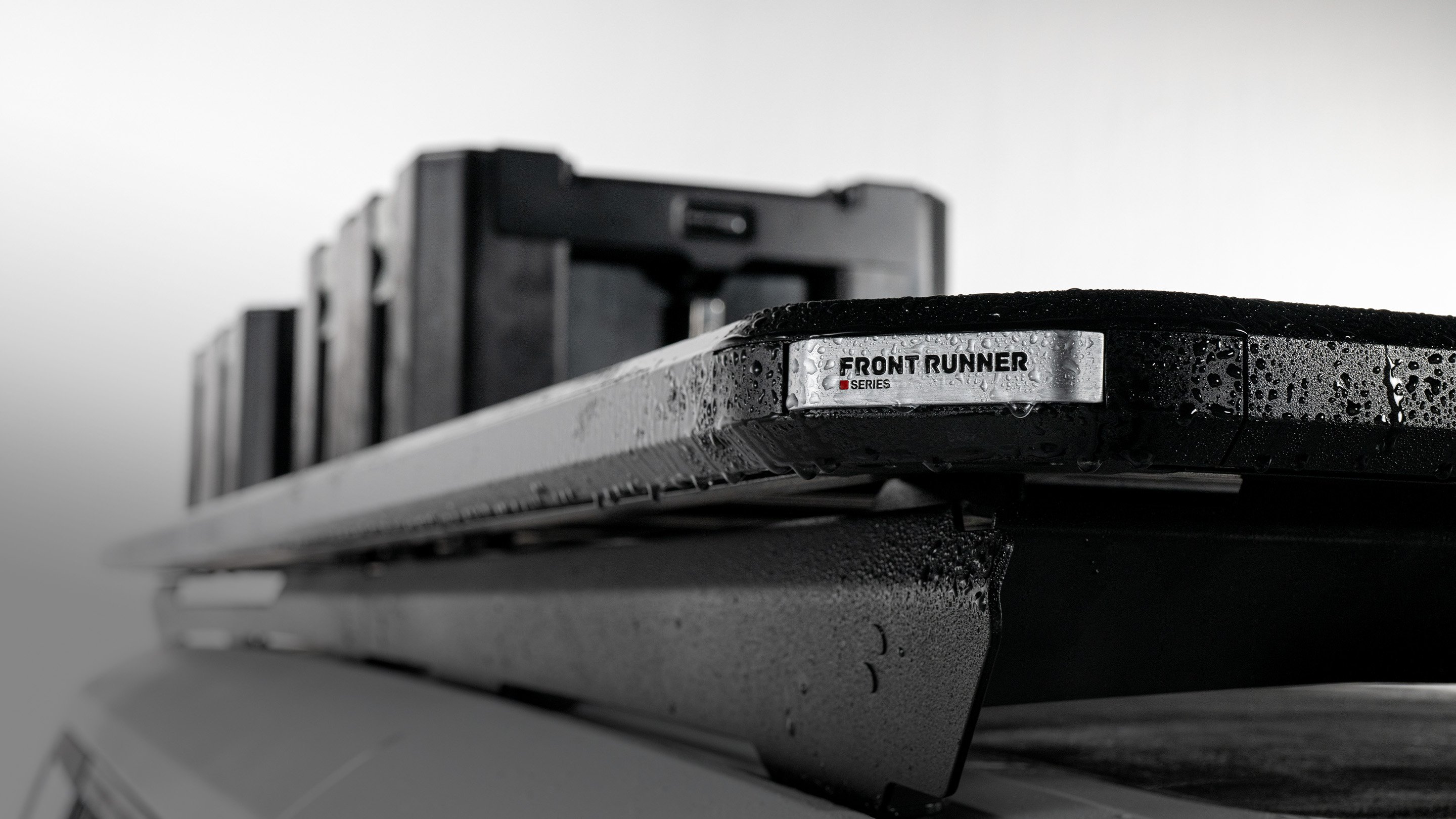 Front Runner Series Slimline 3 roof rack mounted on a vehicle roof, shown in close-up with water droplets highlighting its low-profile aluminum design.