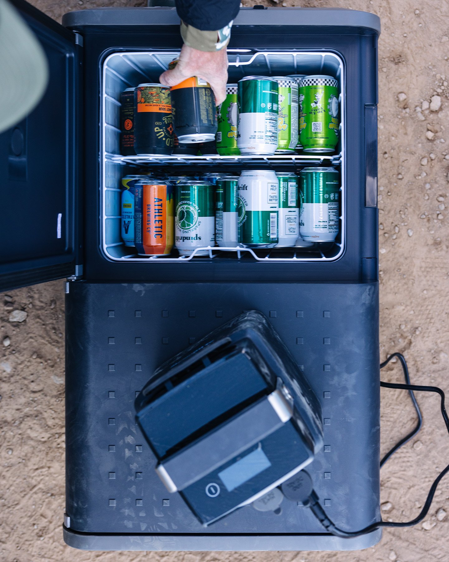 Dometic CFX5 kompressorkylbox öppen uppifrån med dryckesburkar, portabel elektrisk kylbox ansluten till ström på marken
