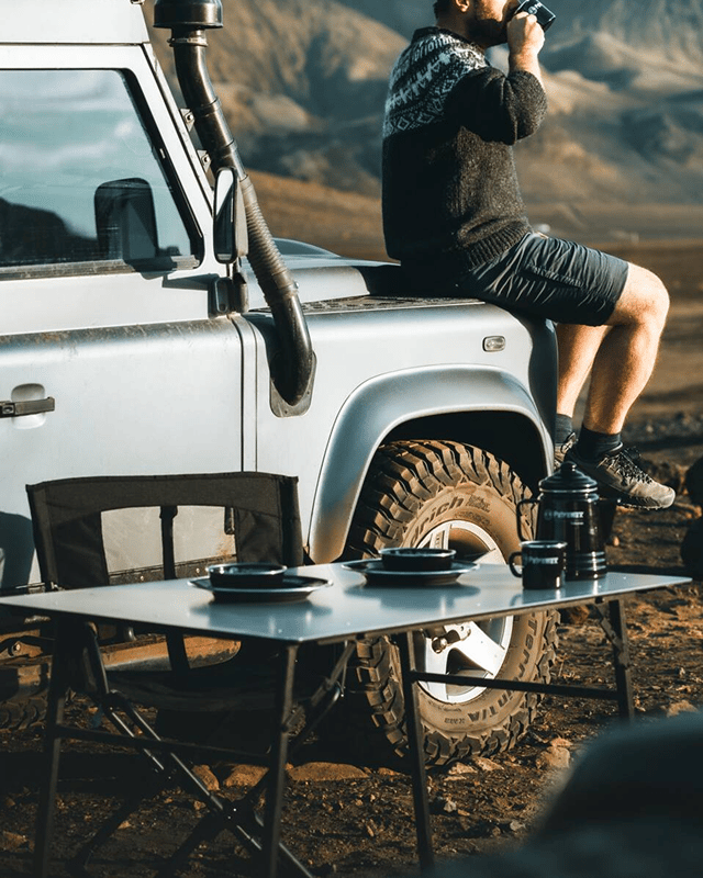 Camp table with plates and chairs in front of jeep.