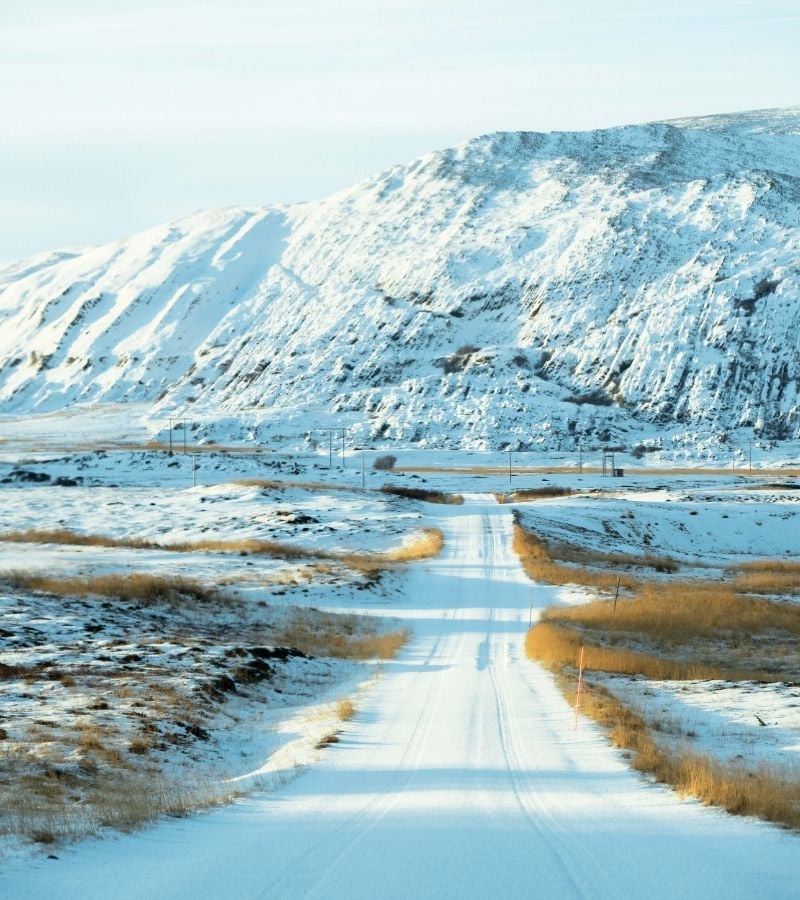 A remote winter scene with snow-covered road stretching into the distance and icy mountains in the distance.