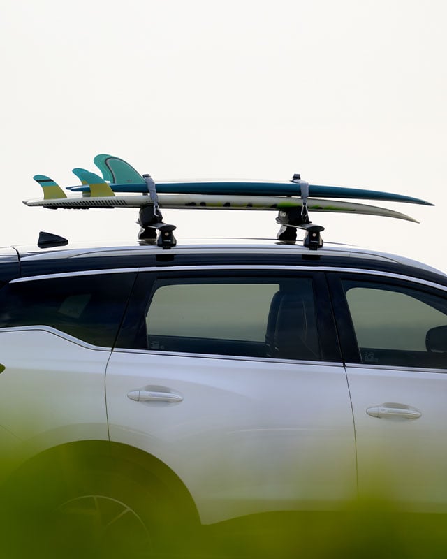 Surfboard secured to load bars with a tie-down strap, showcasing roof-mounted gear transport for outdoor adventures