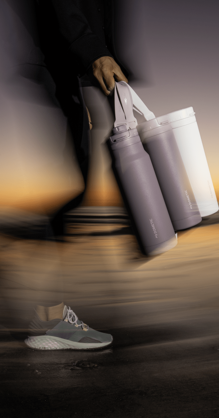 Person walking holding purple and white drinkware items by straps.