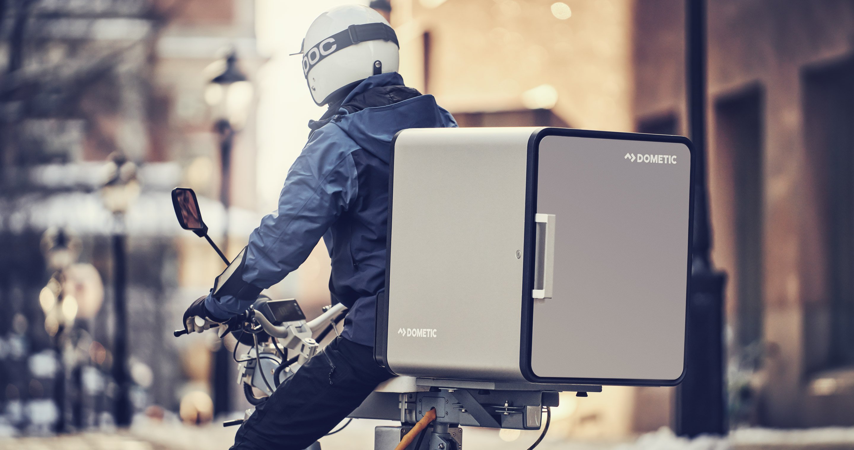 A man riding motor bike with a close up of a Dometic cooler on the back of the bike.