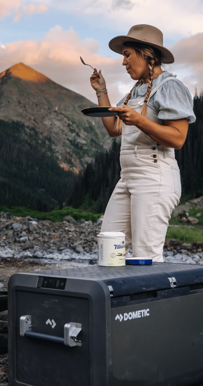 woman at campsite with cooler in foreground and mountains in background