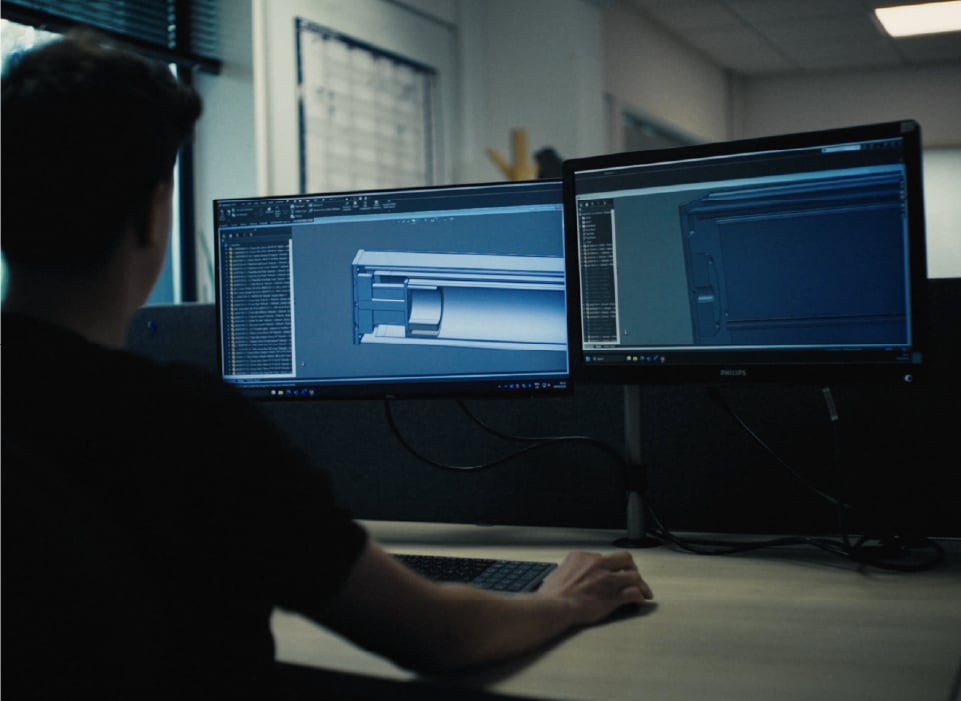 A person wearing a dark short-sleeved shirt sits at a desk with two computer monitors