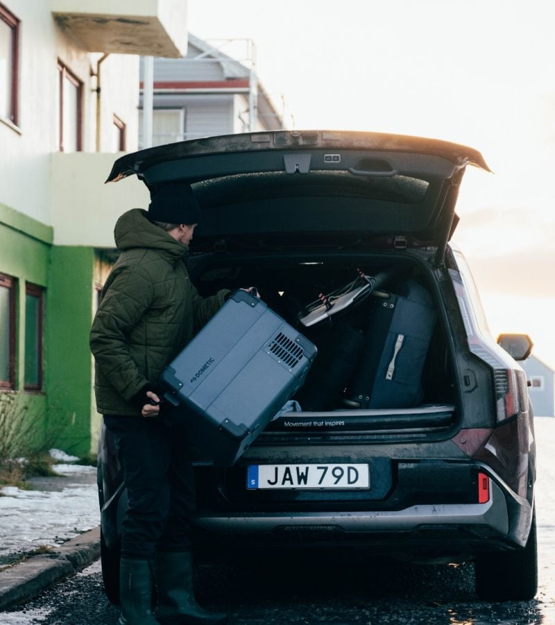 A person loading or unloading a portable fridge into the back of SUV