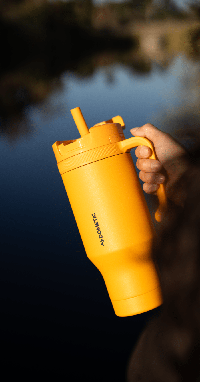 Yellow travel tumbler at sunset with tall grass background