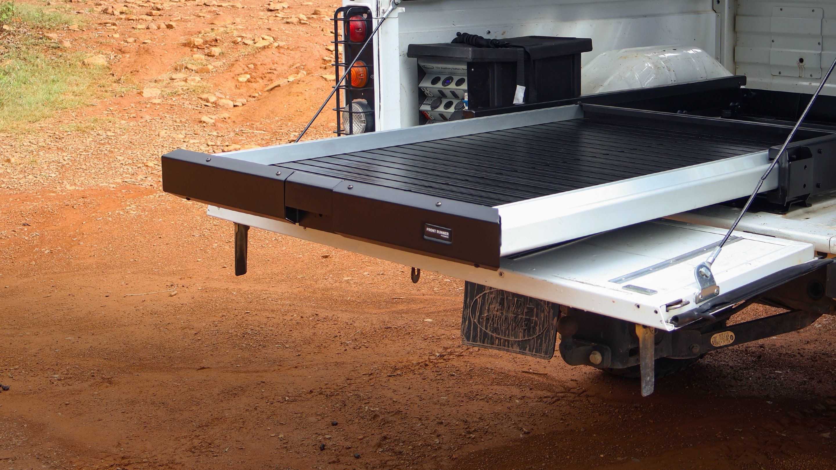 Front Runner Dometic cargo bed slide fully extended from the rear of a pickup truck, creating a flat sliding load surface in an outdoor setting.