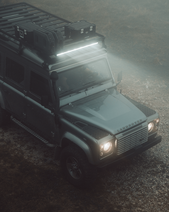 Galerie de toit avec barre lumineuse LED et boîtes de rangement montées sur un Land Rover Defender, éclairée dans des conditions tout-terrain de faible luminosité