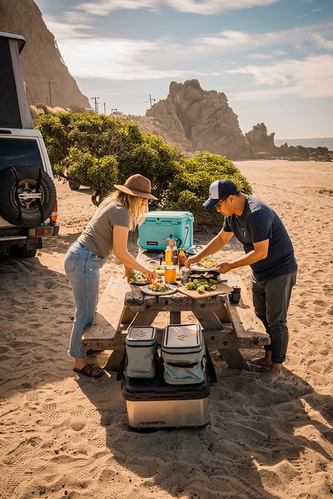 A couple preparing food on a picnic table with Dometic coolers. 
