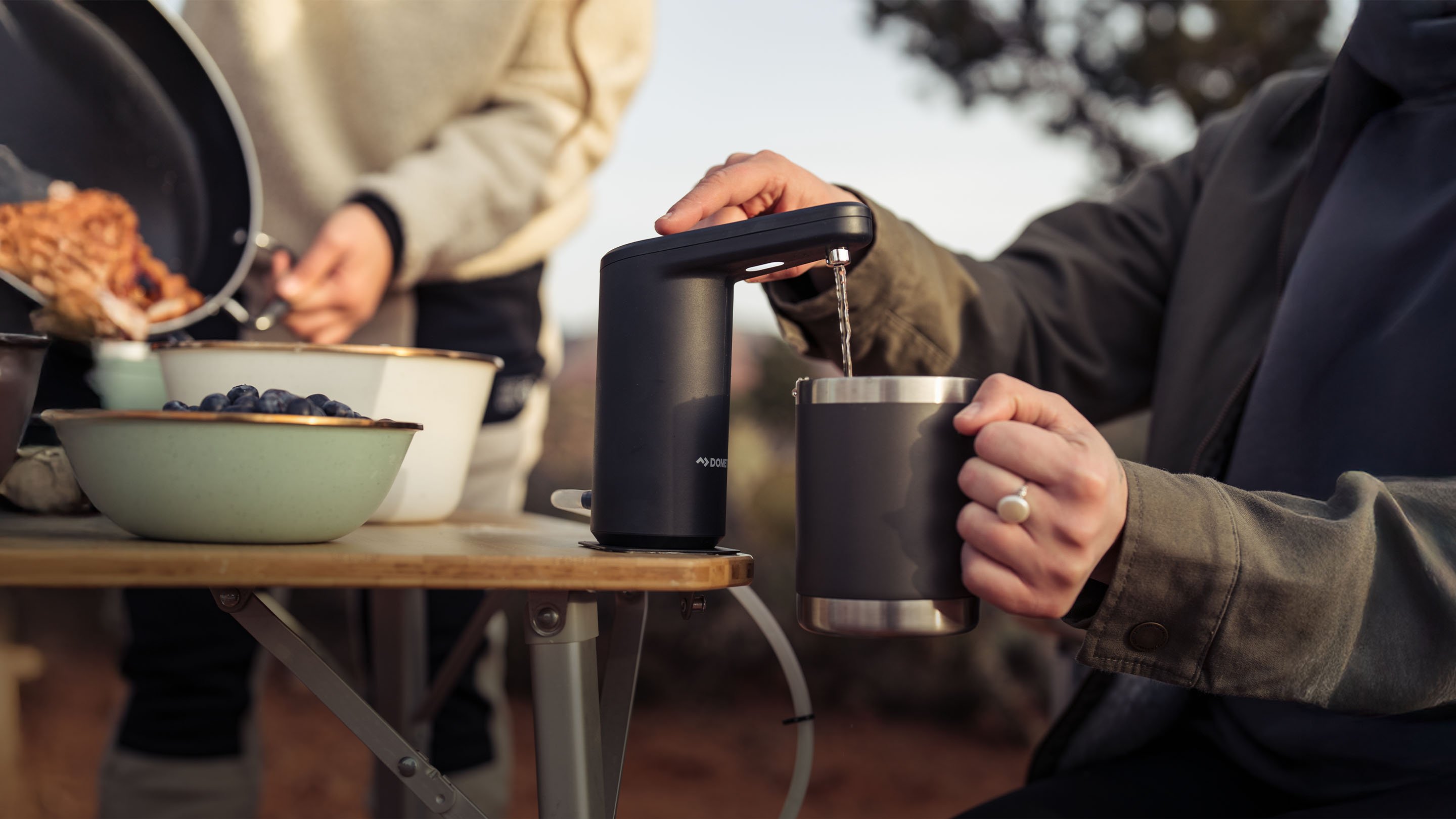 Dometic GO Hydration Water Faucet dispensing water into an insulated mug at a campsite, portable water solution for outdoor adventures