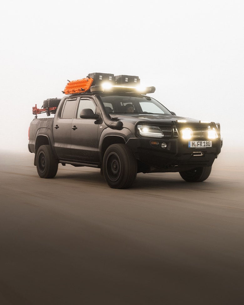 Pick-up équipé d’une galerie de toit, d’une barre lumineuse LED, de plaques de désensablage et de boîtes de rangement roulant dans des conditions tout-terrain poussiéreuses
