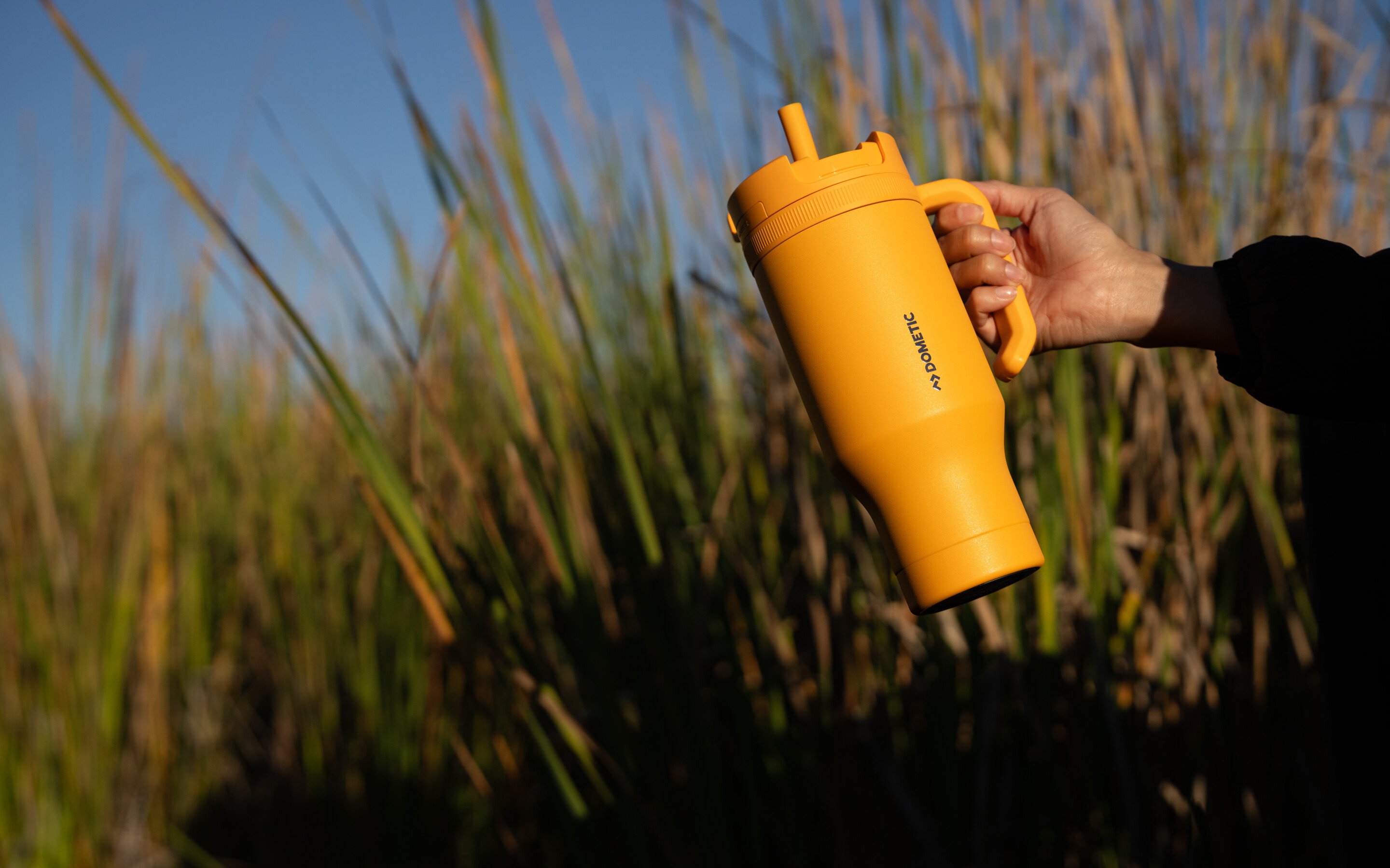 Yellow travel tumbler at sunset with tall grass background