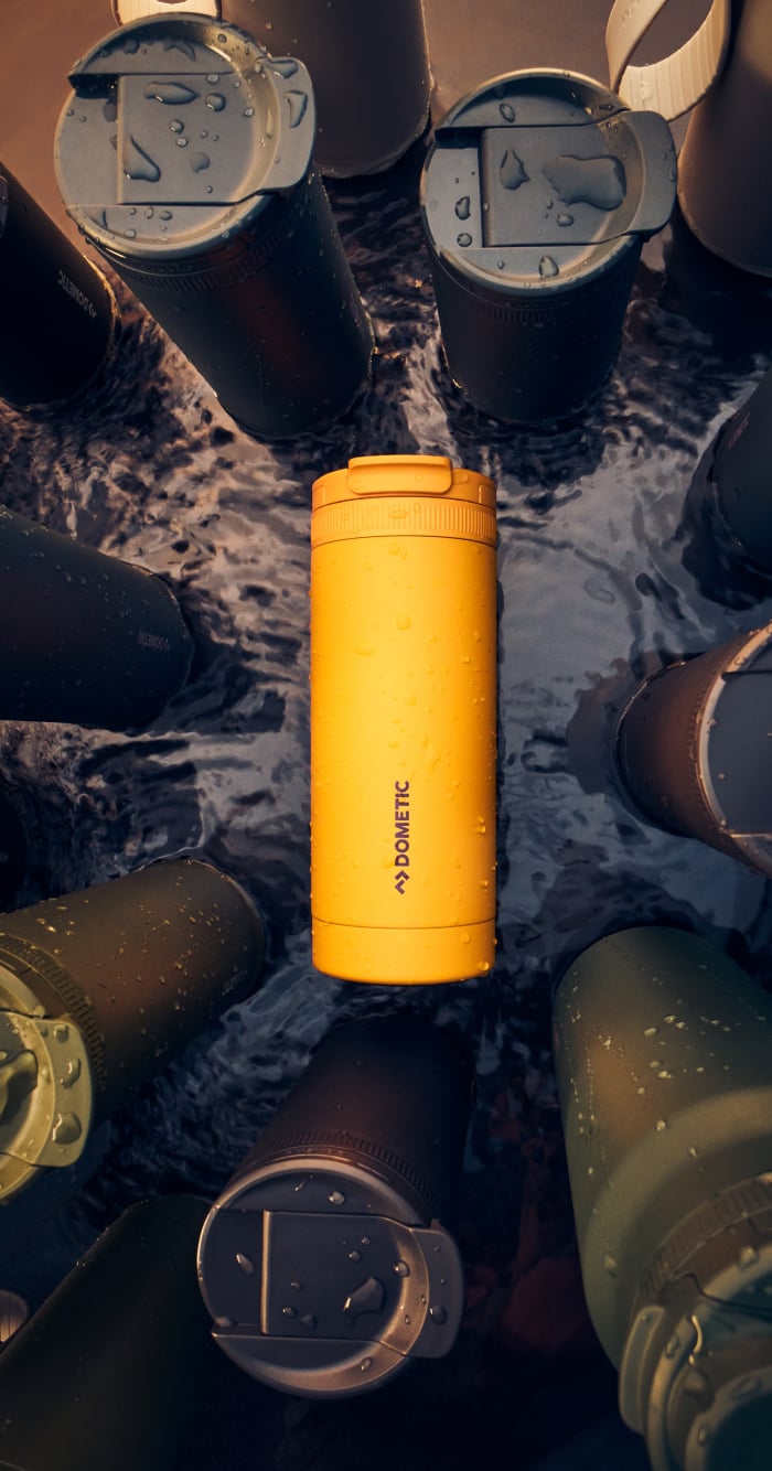 Bright yellow Dometic thermo tumbler lying in water among dark insulated bottles, highlighting durable and outdoor-ready design