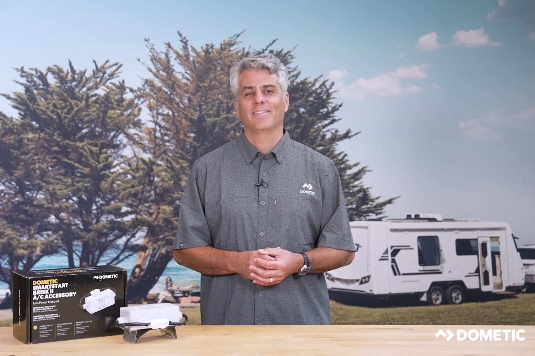 Man posing in front of Air Conditioner item on top of a table, with scenic backdrop behind him.