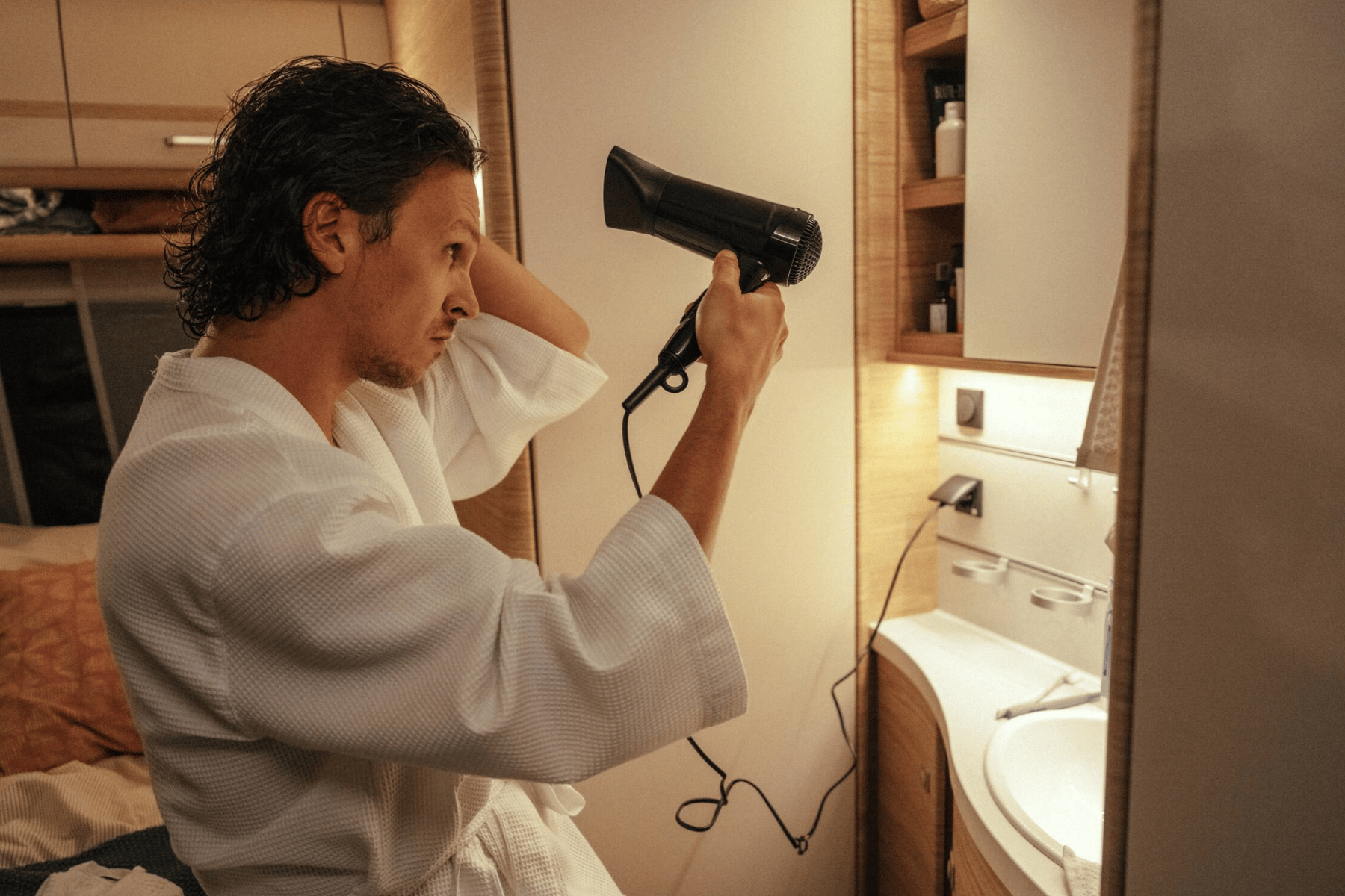 Man with bathrobe on blowdrying hair inside rv.