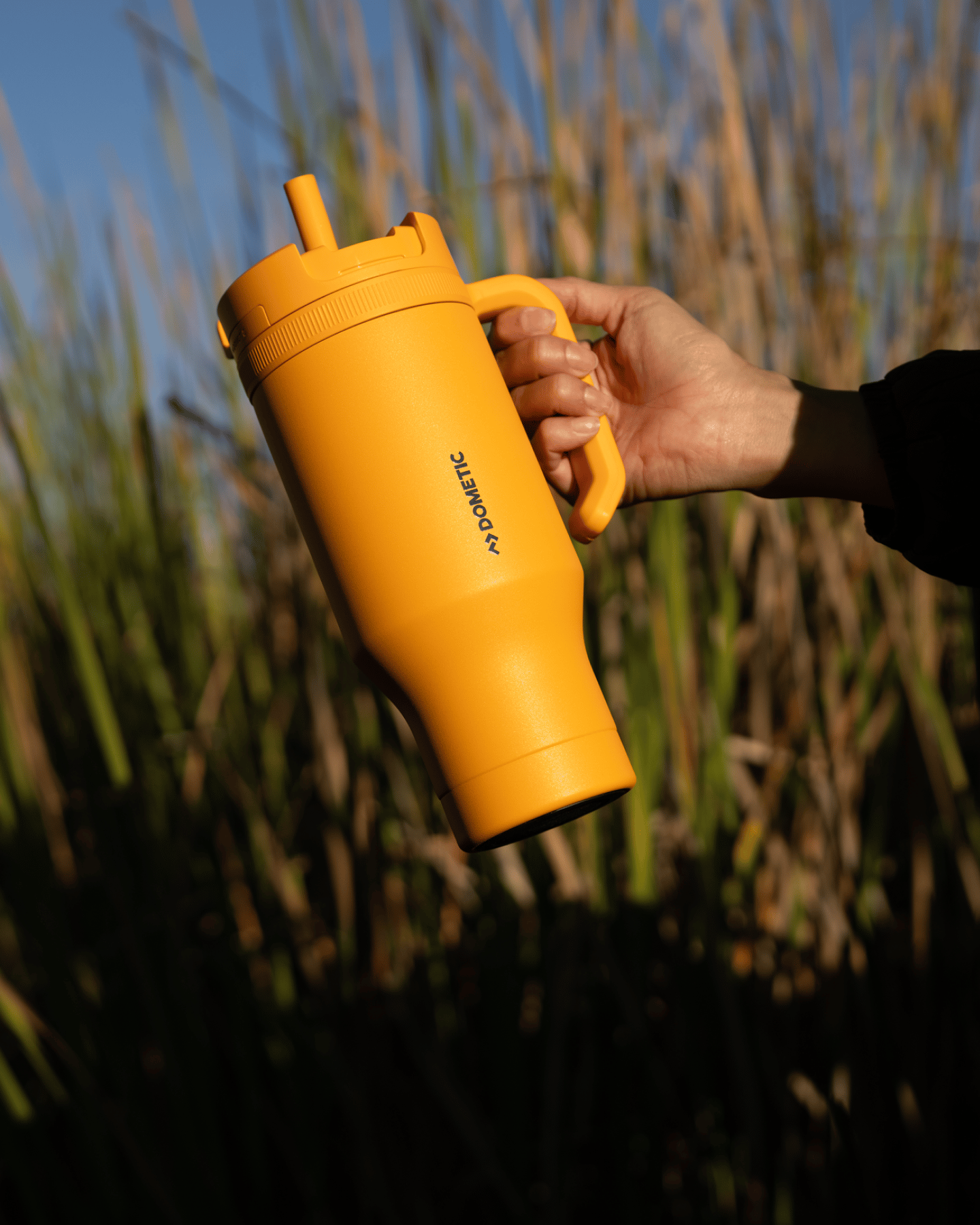 Orange tumbler held in hand in front of marshlands