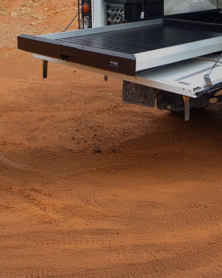 Front Runner Dometic cargo bed slide fully extended from the rear of a pickup truck, creating a flat sliding load surface in an outdoor setting.