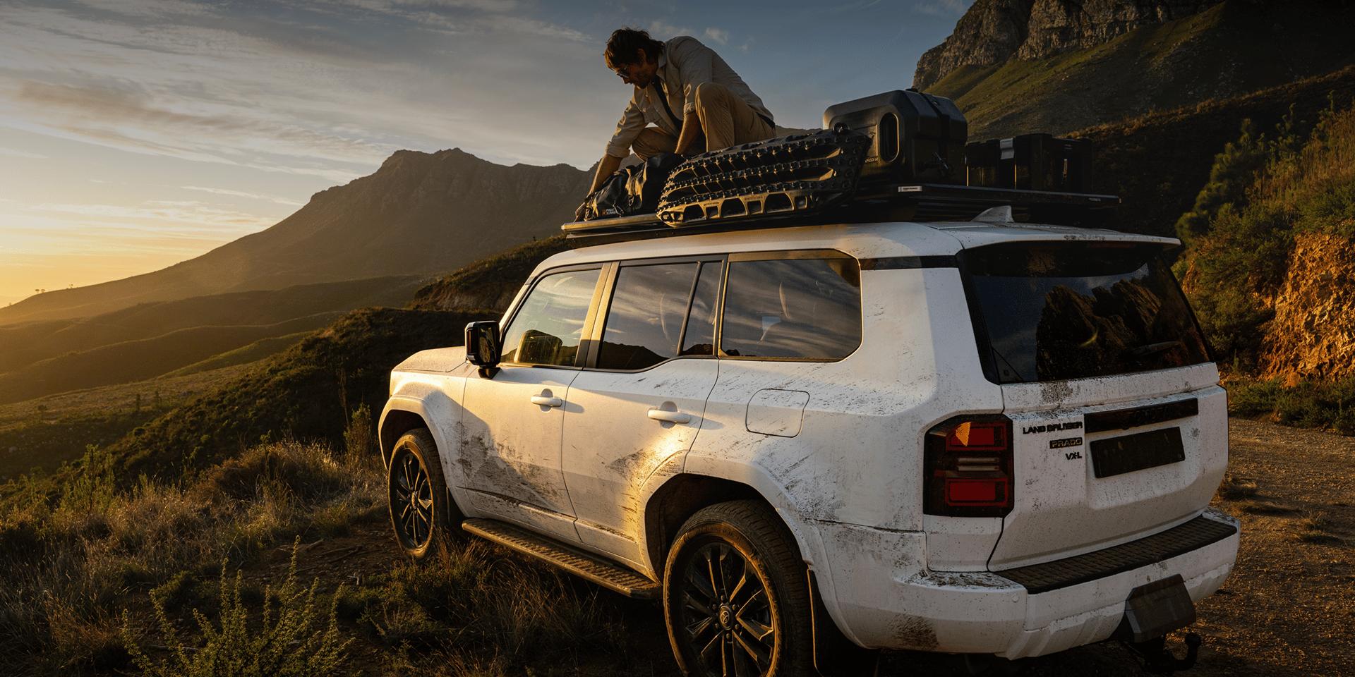 Land Cruiser Prado covered in dirt and grit from exploring the great outdoors, man adjusting his load on his Dometic Slimline 3 roof rack.