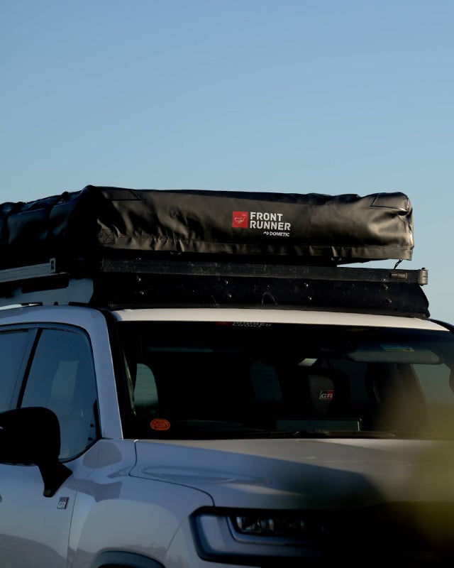 White vehicle with a folded Front Runner Dometic rooftop tent mounted on the roof rack in an outdoor setting.