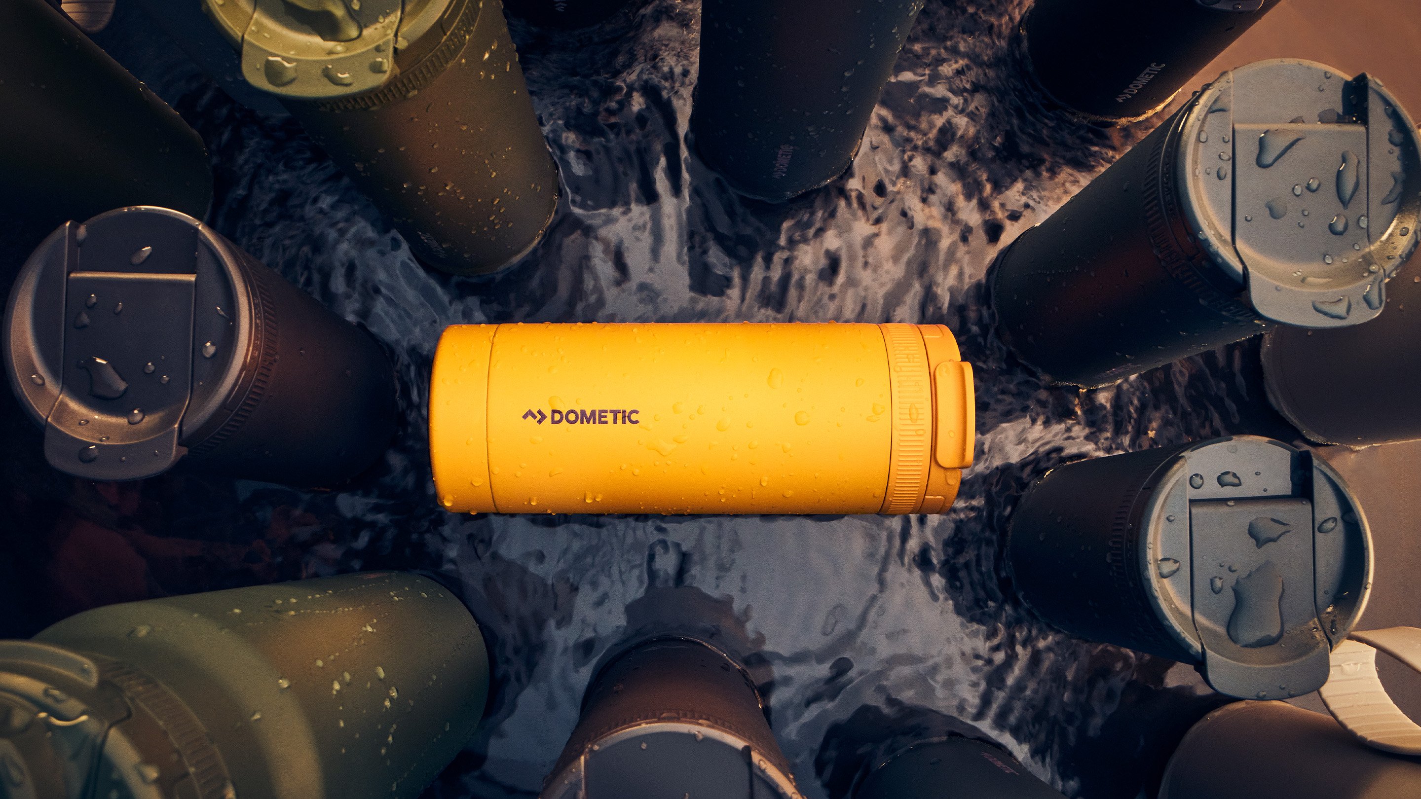 Gul Dometic-termosmugg i vatten omgiven av mörka isolerade flaskor, som framhäver hållbar design för utomhusbruk.